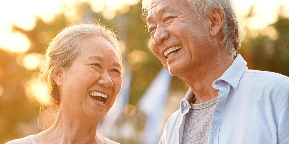 Two older adults smile as the sunlight shines behind them.
