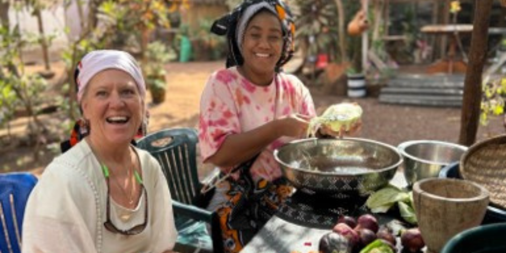 Two women sit outside in Africa preparing a meal at a table.