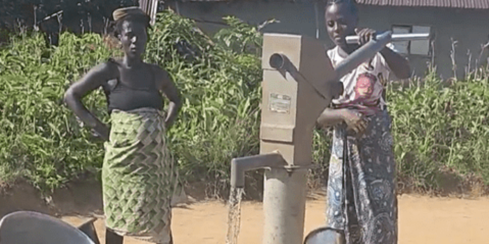 Two women stand at a water pump in Liberia.