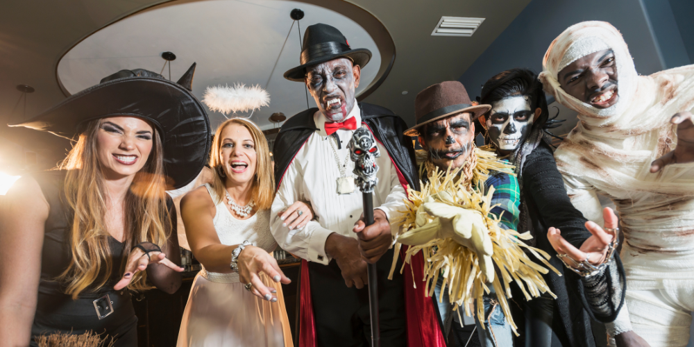 People dressed in Halloween costumes: a witch, an angel, a vampire, a scarecrow, a skeleton, and a mummy.