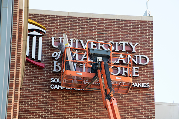 A person cleaning the University of Maryland Baltimore sign