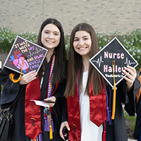 Two graduates displaying their graduation caps.