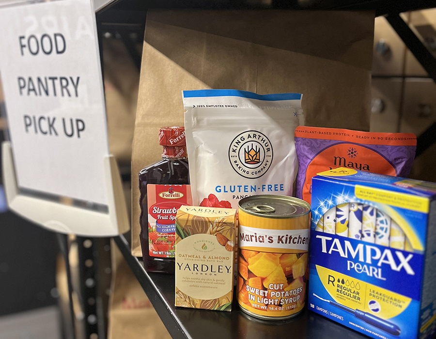 Food items and necessities on a shelf, next to a sign that reads Food Pantry Pickup