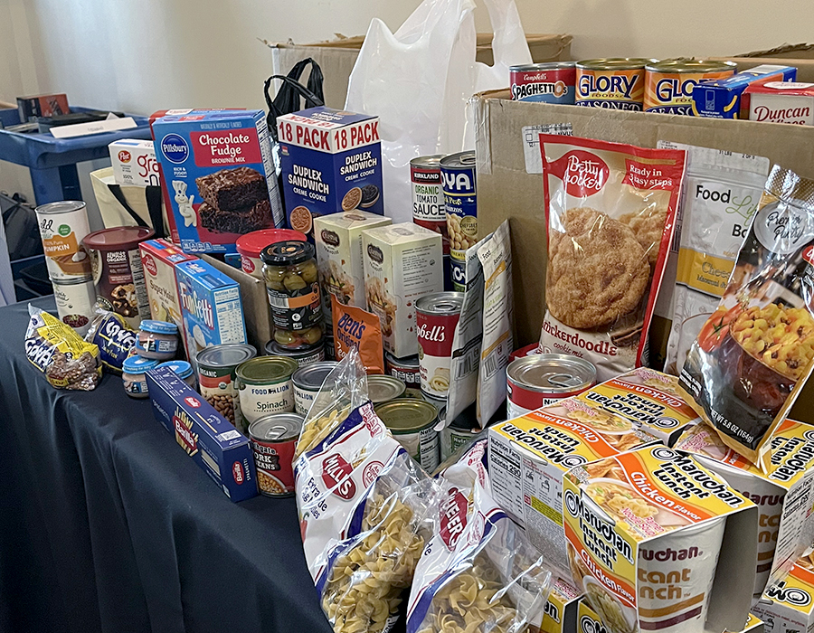 A table overflowing with donated food, including pasta, ramen, baking supplies, canned soup and vegetables, and more