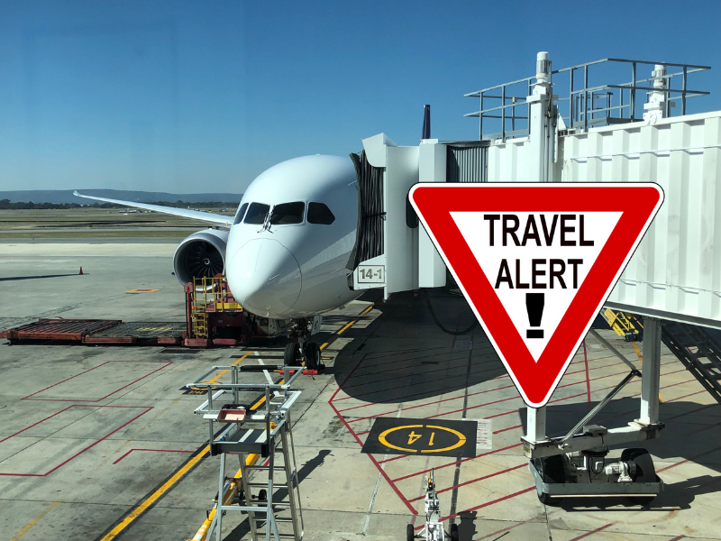 An airplane at the gate with a Travel Alert sign