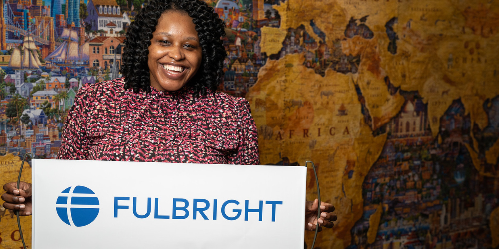 Photo of Abaneh Ebangwese holding a Fulbright banner in front of a world map puzzle
