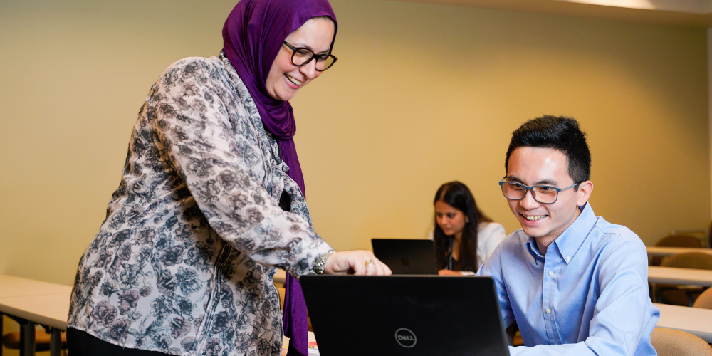 Dr. Danya Qato works with a student on a laptop