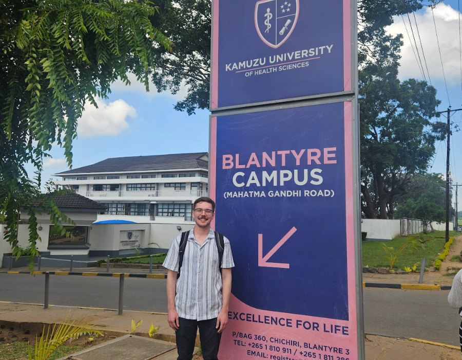 SGS student Jonathan Lawton poses in front of a sign for Kamuzu University's Blantyre campus